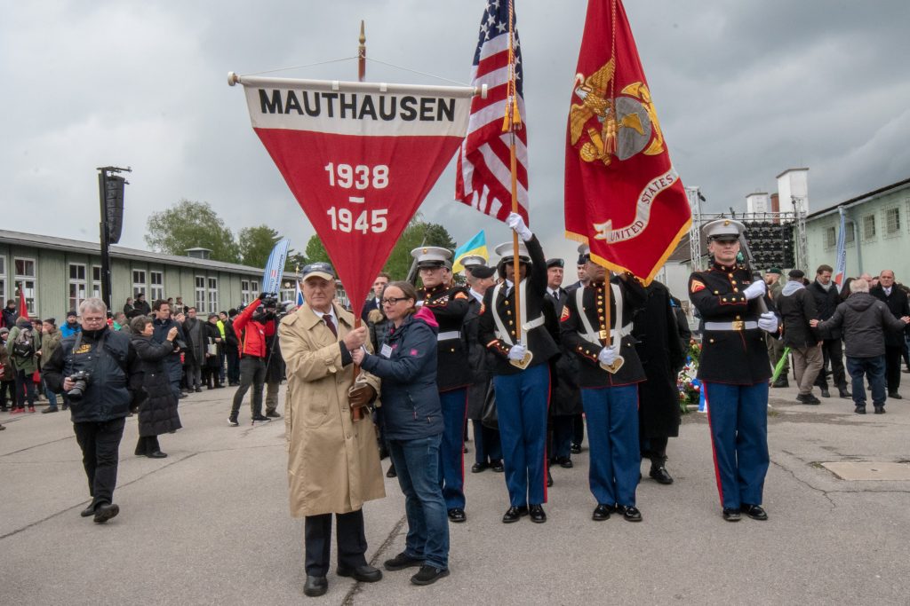 Survivors carrying the flag of the Mauthausen concentration camp followed by US Marines and thousands of people leaving the Mauthausen concentration camp memorial.